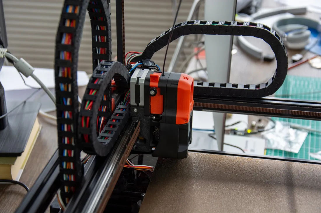 Seitliche Nahaufnahme des roten und schwarzen Voron-Druckkopfs mit Motor, Zahnriemen und Kabelkette.